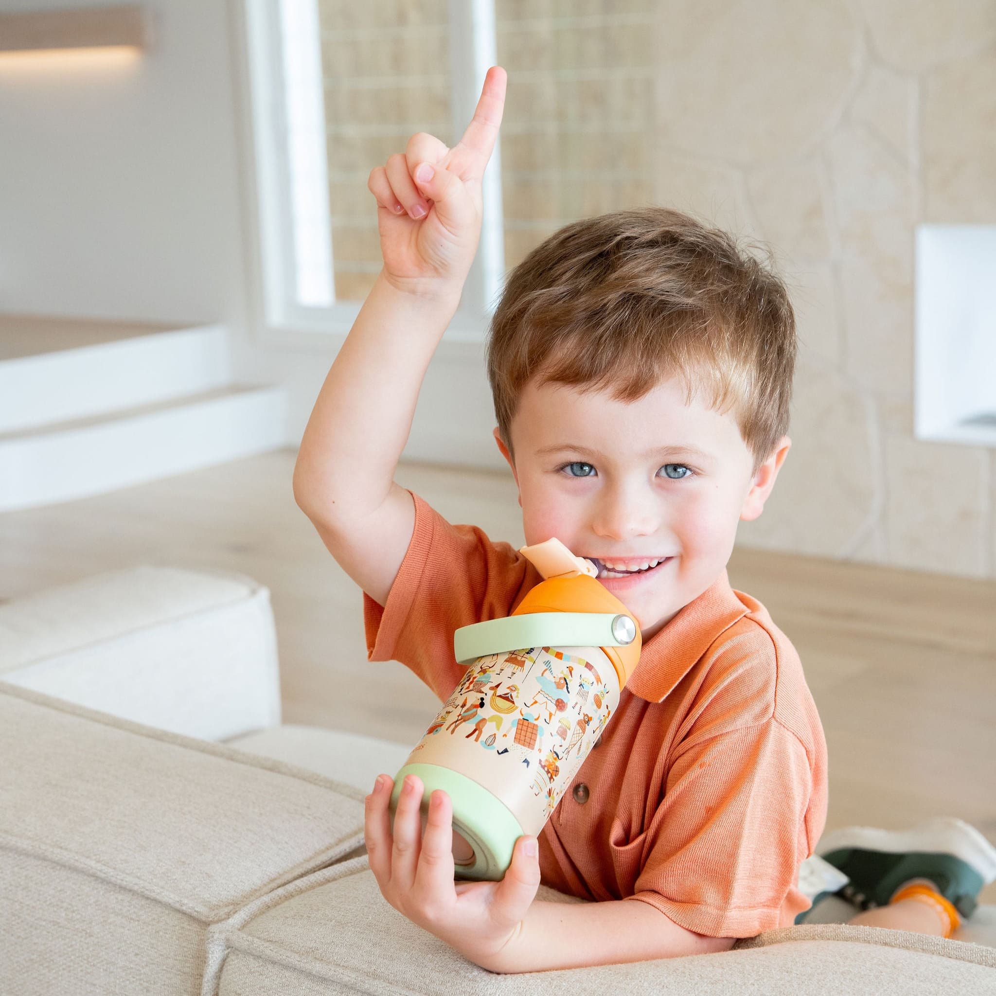 Child holding a colorful bottle and pointing upwards in a home setting