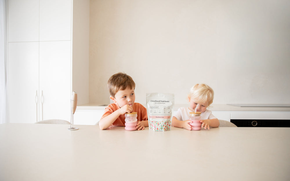 Two boys drinking pink milkshakes at the kitchen bench